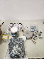 Overview of lot showing packages of screws, large container of nails, metal fittings, and hardware pieces on table