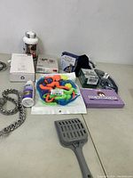 Photo of various new pet care items on a table including dog shampoo, toys, supplements, chain collar, and scoop