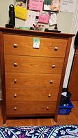 Front view of 5 drawer wooden dresser, showing cherry finish, silver round knobs, and some wear.