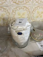 Clear Bohemia Crystal ice bucket with two side handles, displayed with a label inside and placed on a marble surface with vintage tile background.