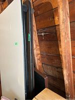 Upright view of folding table with brown top and metal legs, stored leaning against a wooden structure