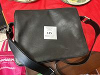 Front view of black genuine leather messenger bag with shoulder strap laid out on a wooden surface.