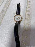 Gold-tone wristwatch with black leather strap and 35 emblem on dial on striped fabric background.