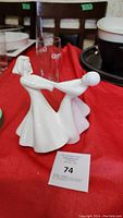 Side view of the white Royal Doulton figurine showing two women holding hands in a dance pose on a red cloth background.