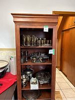 Tall wooden shelving unit filled with assorted silver-plated items including drinkware, trays, and serving pieces.