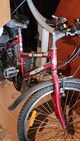 Side view of red Supercycle bike showing frame, front wheel, pedals, saddle, and handlebar.