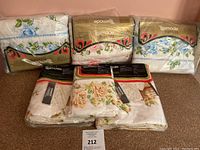 Five bedding items in original packaging with floral designs, including blue and rose patterns.
