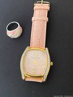 Photo showing pink strap wristwatch with gold-tone rhinestone case and decorative pink/beige rhinestone ring.