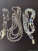 Lot showing three necklaces including carved jade pendant and two beaded strands on black background