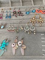 Photo showing a collection of 12 pairs of assorted dangle and drop earrings on a gray velvet organizer.