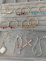 View of five pairs of gold-tone hoop earrings with colored stones and several silver-tone jewelry pieces on a gray jewelry tray