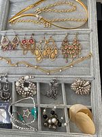 Jewelry assortment showing earrings, bracelets, brooches, and gold-tone necklace in gray fabric organizer
