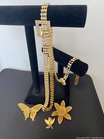 Photo showing lot of gold-tone rhinestone necklaces, bracelet, and brooches displayed on black jewelry display stand and surface.