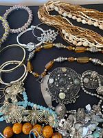 Assorted vintage jewelry pieces laid out on black background showing necklaces, bangles, brooches, and bracelets with various materials and designs.