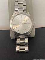 Front view of silver-tone Michael Kors watch on display cushion showing dial and bracelet.