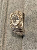 Close up photo showing the left side and top of the sterling silver men's ring with clear oval white Topaz and halo of smaller stones. The textured segmented band is visible.