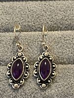 Pair of sterling silver amethyst dangle earrings displayed on gray felt background, showing front and hanging side view with hooks and stopper backs.