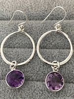 Pair of sterling silver hoop earrings with amethyst gems shown against a grey fabric background.