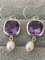 Front view of sterling silver amethyst earrings with pearl drops on grey textile background