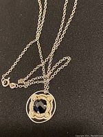 Close-up front view of sterling silver chain with round pendant featuring faceted black onyx center and small clear stones on ornate frame.