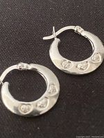 Pair of sterling silver hoop earrings on black background showing the front side with heart and CZ details