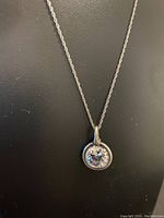 Photo of the full necklace on a black background showing the twisted rope chain and round pendant with clear cubic zirconia stone.