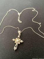 Sterling silver chain necklace with detailed cross pendant featuring multiple cubic zirconia stones on black background.