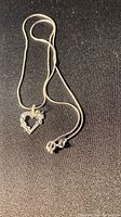 Necklace laid out flat showing the heart-shaped pendant with floral design and chain clasp.