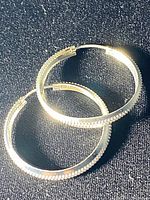 Pair of sterling silver hoop earrings on a dark fabric background showing the textured pattern and clasp closure.