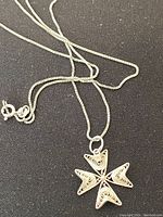 Sterling silver necklace with filigree cross pendant shown on a black background, highlighting the pendant's wire coiled design and chain clasp.