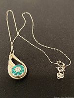 Full view of sterling silver necklace with pendant showing turquoise inlay and clear stone on chain, on black background.