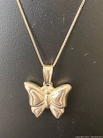 Close-up of butterfly pendant on chain against black background.
