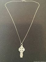 Full view of sterling silver necklace with intricate cross pendant on thin chain.