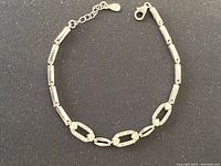 Front view of sterling silver necklace laid flat on black surface showing rectangular and decorative links including heart and crystal embellishments.