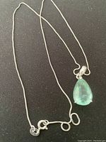 Sterling silver necklace with light green pear-shaped faceted gemstone pendant and a fine chain with clasp, laid on dark surface.