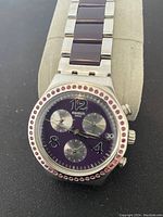Front view of Swatch wristwatch showing purple dial with chronograph subdials, crystal bezel, and date window.