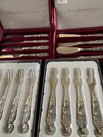 Four boxed sets of vintage silver-tone flatware and cutting tools with ornate handles, some with gold-tone blades.