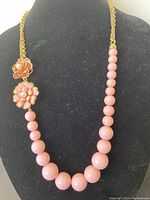 Front view of vintage pink bead necklace with gold-tone flower charms worn on black display bust