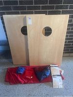 Two solid wood cornhole boards standing upright showing circular holes, with red carrying bag and bean bags placed in front.