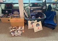 Full lot overview showing plastic bin with coasters, folded chairs, boxes of magazines and ticket stubs on floor