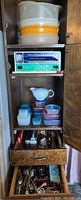 Full view of kitchen cabinet with stacked plastic containers, box of foil, and drawer of utensils