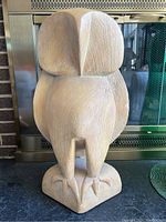 Front view of large mid century owl sculpture showing texture and damage near the head and wings, with fireplace background.