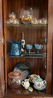 Full view of barware and vintage items displayed inside a wood cabinet. Contains glass and pottery pieces on three shelves.