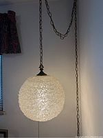 Full view of the hanging swag light showing clear spun glass sphere and chain