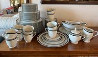 Full view of Noritake Horizon dinnerware set, showing stacked plates, several cups with saucers, creamer, sugar bowl with lid, gravy boat, and serving dishes on wooden surface.