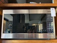 Full frontal view of the Panasonic microwave showing stainless steel finish, glass door, control panel with keypad and display screen, and a label showing 'Inverter' technology.