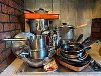 The entire collection of pots, pans, kitchen utensils, and cookware stacked on a stove top and counter.