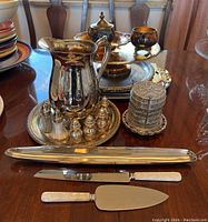 Photo showing large silverplate pitcher, salt and pepper shakers on tray, spice tower, serving tray, and white handled serving knives