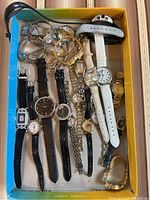 Photo showing entire collection of wristwatches and some bracelets inside a cardboard box on a striped fabric surface