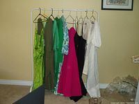 Photo of 10 assorted women's dresses hanging on a white garment rack, showing variety of colors including green, pink, black, white, and floral.
